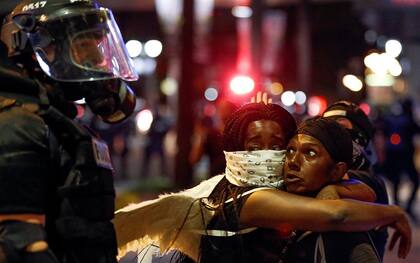 Dos mujeres se abrazan frente a un policía en la madrugada de ayer en Charlotte, Carolina del Norte