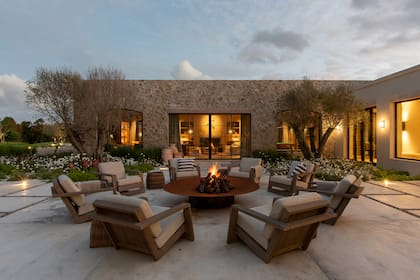 Dos olivos de 90 años, rodeados de canteros floridos. Los sillones, de teca, rodean el fogonero hecho especialmente para este espacio.