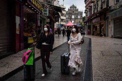 Dos turistas caminan con su equipaje en el centro histórico de Macao