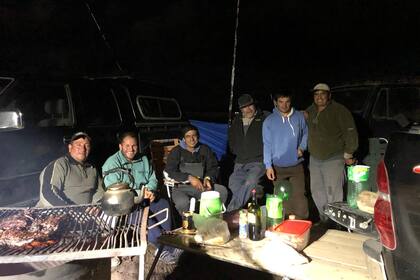 Durante la noche, un equipo de pescadores amigos, oriundos de la zona, comen un asado y descansan, mientras las cañas continúan en los haraganes a la espera del pique; uno de ellos, Natalio Dualde, de gorra y buzo negro, ha participado en 45 concursos ininterrumpidos
