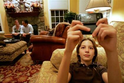 Dylan Herina, de 13, manda mensajes de texto, con sus padres Beth y Peter de fondo. Las nuevas tecnologías plantearon desafíos a las normas de convivencia familiar.