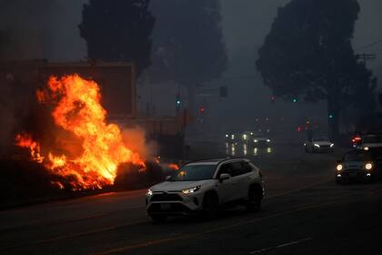 ehículos pasan junto a las llamas del incendio mientras abandonan la zona.