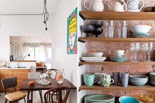 Mesa antigua de madera maciza y sillas vintage, acompañadas por una obra de Guille Pachelo. El acceso al cuarto principal desde la cocina se cerró con un muro de ladrillo. En la superficie ganada se armó una estantería.