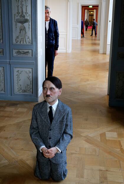 El artista italiano Maurizio Cattelan posa junto a su obra de arte 'Él', que representa a Hitler de rodillas en oración antes de la inauguración de la exposición "Sin miedo al amor" en el Hotel de la Monnaie el 17 de octubre de 2016 en París, Francia. La obra fue subastada y se vendió por 17,2 millones de dólares