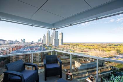 El balcón, cuadrado, con un juego de sillones de exterior, se funde con el interior del departamento a través de sus paredes totalmente vidriadas