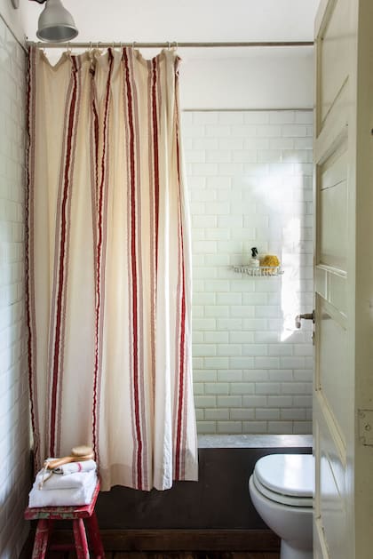 El baño en suite tiene bañadera de cemento alisado, revestimiento de azulejos esmaltados y cortina en tussor en juego con el cubrecama.