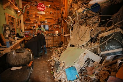 El barbero Mohammad Mehdi le corta el cabello a su cliente Ayman Al Zein dentro de su barbería, que resultó dañada en un ataque aéreo israelí que también dañó el local de Al Zein, en Dahiyeh, en los suburbios del sur de Beirut, Líbano