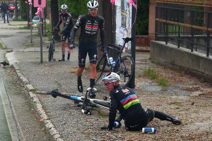 El belga Remco Evenepoel está en el piso, lamentándose por la situación inesperada, mientras dos compañeros se acercan a asistirlo, en la quinta etapa, Atripalda-Salerno.