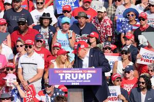El candidato presidencial republicano Donald Trump al recibir el disparo del tirador en su oreja derecha. Atrás a su derecha se ve a una mujer de gorra negra y anteojos de sol que se queda quieta frente al hecho (REUTERS/Brendan McDermid)
