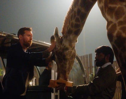 El capitán de la selección argentina acariciando a una jirafa, mientras un lugareño supervisa la actividad