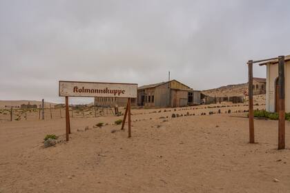 El cartel de Kolmannskuppe en German Kolmanskop - Ciudad fantasma de Kolmannskuppe en Namibia con los edificios abandonados en el desierto de Namib
