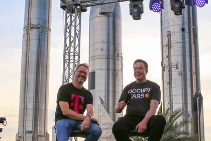 El CEO de T-Mobile junto a Elon Musk, fundador de SpaceX; detrás suyo, un prototipo de Starship, el cohete que permite salir de la órbita terrestre para llegar a la Luna y con el que planea ir a Marte