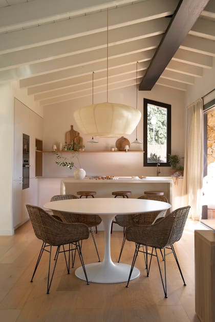 El comedor apuesta por lo simple: una mesa circular blanca con sillas de ratán, iluminadas por una gran lámpara de papel de arroz, que aporta frescura y una ligereza visual y refuerza la estética mediterránea del conjunto.