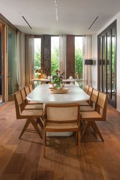 El comedor, con mesa laqueada de poro abierto y sillas de esterilla natural y madera, todo cápsula de Algodón House