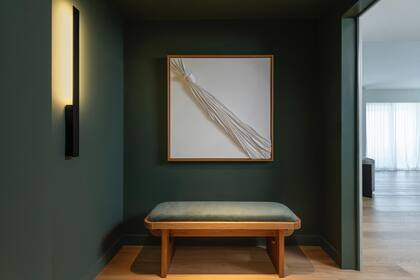 El cuadro, hecho a medida y pensado exclusivamente para ese espacio, por Gabriela Herman. Banco (Taller Ferro) y aplique de pared (Dimm). El color en la pared, Rosemary (SW6187, Sherwin Williams).