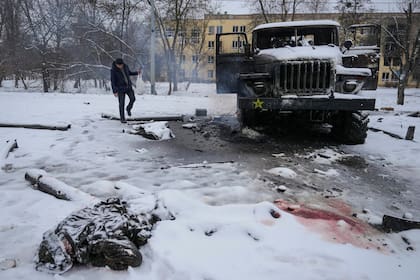 El cuerpo de un militar está cubierto de nieve mientras un hombre toma fotos de un vehículo lanzacohetes múltiple del ejército ruso destruido en las afueras de Kharkiv, Ucrania, el 25 de febrero de 2022