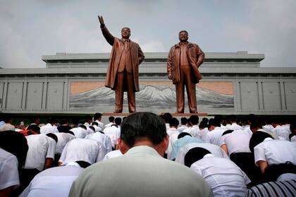 Norcoreanos rinden tributo y flores a las estatuas de bronce de los fallecidos ex líderes del régimen comunista, Kim Il-Sung (izq.) y Kim Jong-il, abuelo y padre de Kim Jong-un, respectivamente