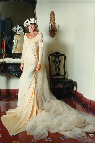 El diseño que Ginette Reynal usó en su boda con Julio Zavaleta, el 27 de abril de 1986, se convirtió en un traje icónico y uno de los más copiados. En esta ocasión, y con la complicidad de la novia, Gino se decantó por un diseño totalmente lánguido, dado que la estatura, los hombros y la fuerza de la cara de la modelo lo permitían, al que le dio su toque con la inmensa y larguísima cola de tul y el tocado de flores de seda que caían sobre la espalda.

