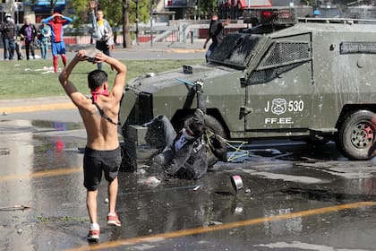 Un vehículo de las fuerzas de seguridad arrastra a un manifestante mientras otro le arroja piedras