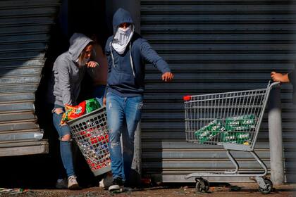 Dos manifestantes salen con un canasto lleno de mercadería de un supermercado que fue saqueado en Santiago de Chile