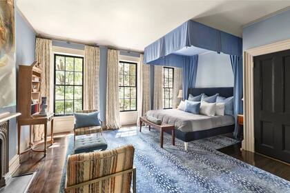 El dormitorio principal cuenta con otra chimenea de leña, techos altos y tres ventanas que ofrecen vistas al jardín