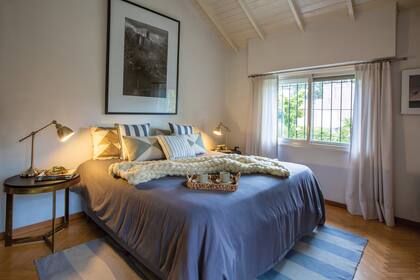 El dormitorio principal. La manta tejida a mano y la alfombra de lana suman calidez en esta mañana fría. Aprovechando los techos altos, Sebastián enmarcó una fotografía XL de un lago de Londres que compró en un viaje.