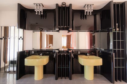 El espejo revela que el baño está auténticamente en suite, sin división alguna con el dormitorio. Superficies esmaltadas en negro... y en un amarillo tan de la época que merecería un nombre propio.