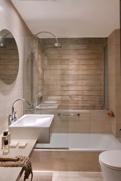 El espejo suspendido, sin marco, parece flotar sobre la superficie mineral y se refleja en los brillos cromados de las griferías