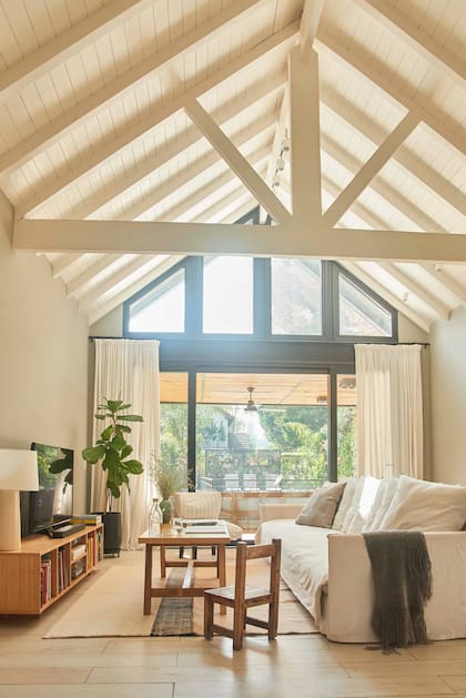 El estar ahora está mejor conectado con el jardín gracias a las amplias carpinterías. Al pintar de blanco el techo de madera original, a dos aguas, le cambiaron el estilo a todo el sector.