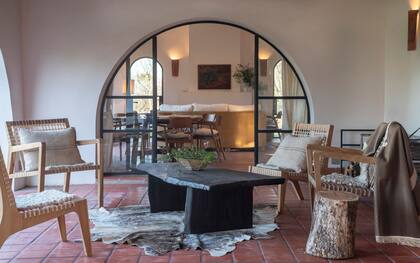 El estar conecta con una galería con mesa ratona en madera quemada (Nanu Cibils) y sillas de tiento (MDS Diseño)