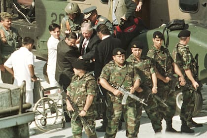 El ex dictador chileno Augusto Pinochet (en el centro, con el cabello canoso) es escoltado desde un helicóptero de la Fuerza Aérea hacia una silla de ruedas en la azotea del Hospital Militar, mientras tropas del Ejército montan guardia, el 3 de marzo de 2000. Pinochet fue trasladado al hospital para realizarse exámenes médicos apenas llegó a Chile. /Photo by Martin Thomas REUTERS