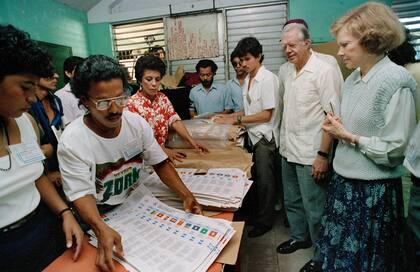 El expresidente de EEUU Jimmy Carter y su esposa Rosalynn, derecha, observan mientras trabajadores electorales preparan boletas en un centro de votación en Managua, Nicaragua, el 25 de febrero de 1990. Los Carter fueron a Nicaragua como observadores electorales.