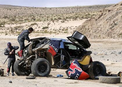 El francés Sebastien Loeb trata de reparar el auto tras el vuelco de ayer