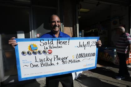 El funcionario de lotería Rick Herrera sostiene un cheque ampliado afuera del Mini Market de Las Palmitas donde se vendió el boleto ganador de la lotería Powerball en el centro de Los Ángeles. (AP Photo/Marcio Jose Sánchez)
