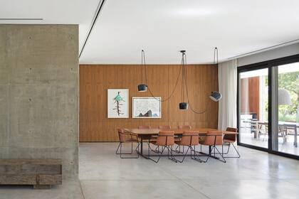 El hall de entrada con banco de madera recuperada (Pablo Ledesma) da paso al comedor con lámpara ‘Aim’ (Flos,Italia). Sobre el revestimiento de petiribí, obras de Matías Duville. Aberturas de aluminio (Marroncelli). Cortinas de tussor (Casa Almacén).