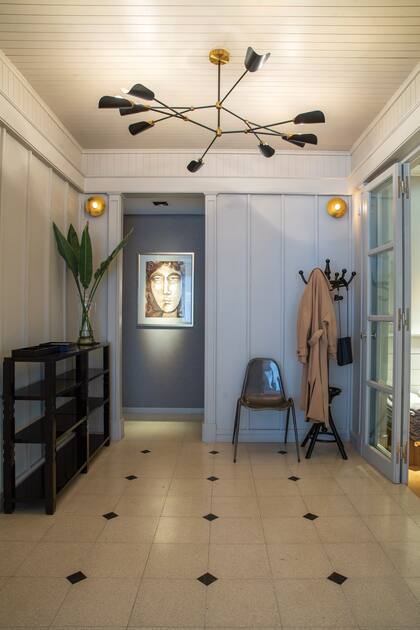 El hall de entrada mantiene la gama cromática de todo el departamento y suma unos guiños de dorado en los apliques y en la lámpara.