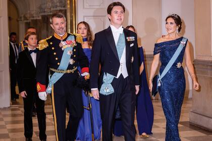 El homenajeado entró a la recepción a paso firme, vestido con un jaquette oscuro, camisa y moño blancos y zapatos negros, y lució una banda azul sobre su pecho y distinciones en la solapa. Detrás de él, su padre, el príncipe real Federico, con uniforme de gala. Su madre, Mary, con un diseño de lentejuelas de escote asimétrico del diseñador Jesper Høvring; clutch satinado de Prada y sandalias de Gianvito Rossi. La princesa llevó, además, la tiara que sus suegros le regalaron para su boda, una pieza de oro blanco, diamantes y perlas.