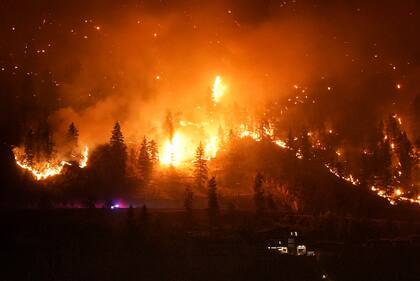 El incendio de McDougall Creek arde en las montañas sobre una vivienda a orillas de un lago en West Kelowna, Canadá, el 18 de agosto de 2023. 