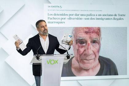 El líder de Vox, Santiago Abascal, en una rueda de prensa con la imagen del anciano agredido de fondo