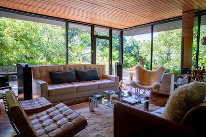 El living, con techos de madera y ventanales generosos con vista al río. En primer plano, dos sillas Barcelona diseñadas por Lilly Reich y Ludwig Mies van der Rohe y, al fondo, una BKF.