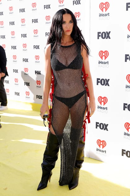 El look de Katy Perry para los premios a la música iHeartRadio dejó poco para la imaginación: un vestido de red, con moños rojos a los costados, que dejaba a la vista su ropa interior negra. Y para completar su atuendo lució unas botas bucaneras