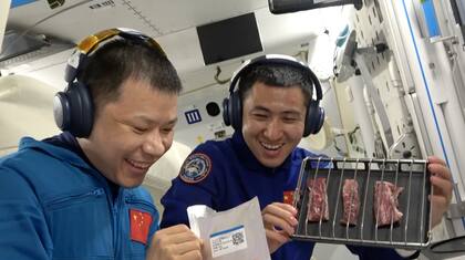 El miembro de la tripulación de Shenzhou 20, el coronel Wang Jie (a la izquierda), y el ingeniero de vuelo espacial de Shenzhou 21, el mayor Wu Fei, se preparan para asar un plato de carne con pimienta negra en un horno especialmente construido, entregado este martes por la nave espacial Shenzhou 21 a la estación espacial Tiangong.