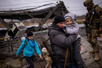 El miliciano local Valery, de 37 años, lleva a un niño mientras ayuda a una familia que huye a cruzar un puente destruido por la artillería, en las afueras de Kiev, Ucrania