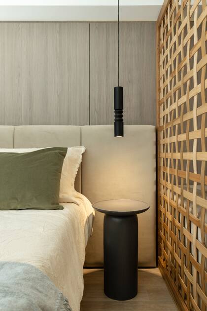 El mismo lenguaje: tanto la mesa de luz como la luminaria son torneadas. El divisor de madera actúa como separador, pero es permeable al paso de la luz.