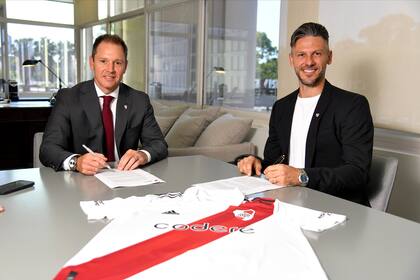 El momento de firmar el contrato con el presidente Brito. Por delante, siempre, la banda roja