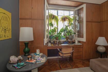 El mueble que reúne espacio de guardado y escritorio es original del departamento, al igual que el revestimiento en es de madera. Sillón y mesa redonda de anticuario. La ventana da al pequeño balcón trasero.