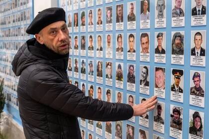 El padre Dmitriev se para en la pared con el retrato de los que murieron y señala al primer hombre de la brigada de sacerdotes que perdió la vida en la guerra (Foto: BBC)