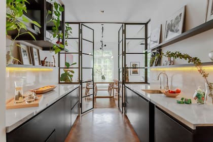 El parquet llega hasta la cocina y la hace parte del espacio social. Más allá del cerramiento, el comedor y las ventanas a Plaza San Martín. Construida en perfilería maciza, la doble puerta se amplía con los paños fijos laterales