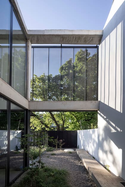 El patio lateral funciona como una extensión del estar, donde apertura y resguardo conviven. Un portón de chapa microperforada y un banco de material acompañan la pantalla semitransparente que filtra luz y miradas.