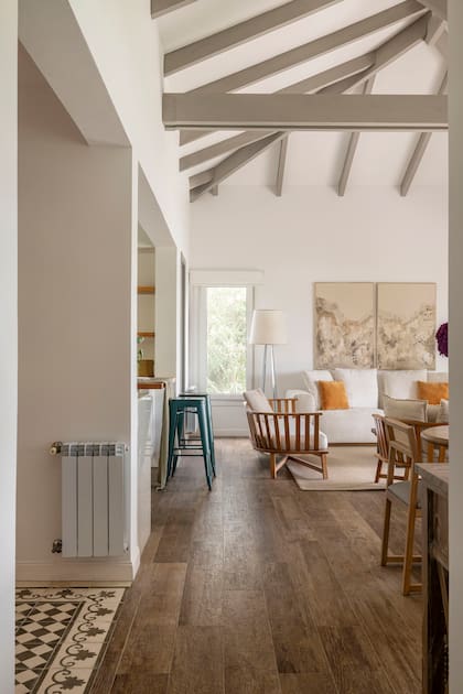 El piso de mosaicos del hall de entrada se encuentra con la madera de la zona social. Las banquetas azules marcan la ubicación de la cocina abierta.